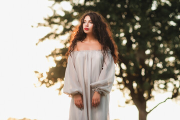 Magnificent volume
curly hair; A dark-haired girl is dressed in a light, light dress; sexy girl posing in the field at sunset; red lipstick on the lips;