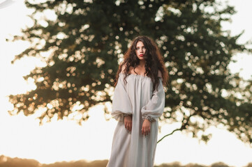 Magnificent volume
curly hair; A dark-haired girl is dressed in a light, light dress; sexy girl posing in the field at sunset; red lipstick on the lips;