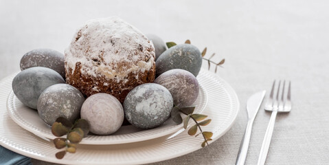 Spring table setting. A plate with a cotton napkin with a bunny, a cake and Easter eggs. Silverware, Easter bunnies and a vase of flowers on a linen tablecloth. The concept of a bright Easter holiday.