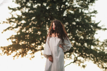 Magnificent volume
curly hair; A dark-haired girl is dressed in a light, light dress; sexy girl posing in the field at sunset; red lipstick on the lips;