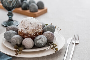 Spring table setting. A plate with a cotton napkin with a bunny, a cake and Easter eggs. Silverware, Easter bunnies and a vase of flowers on a linen tablecloth. The concept of a bright Easter holiday.