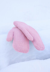 Pink, fluffy mittens are lying on a snow-covered bench. Selective focus.