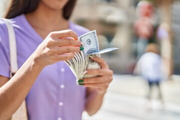 Young beautiful hispanic woman counting dollars at street