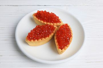 Tartlets with red caviar on a white plate.