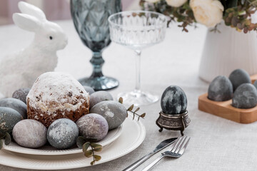 Obraz na płótnie Canvas Spring table setting. A plate with a cotton napkin with a bunny, a cake and Easter eggs. Silverware, Easter bunnies and a vase of flowers on a linen tablecloth. The concept of a bright Easter holiday.