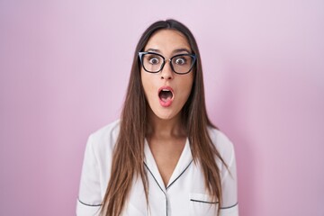 Young brunette woman wearing glasses standing over pink background afraid and shocked with surprise expression, fear and excited face.