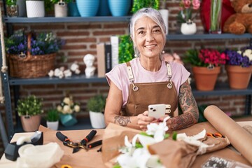 Middle age grey-haired woman florist smiling confident using smartphone at florist