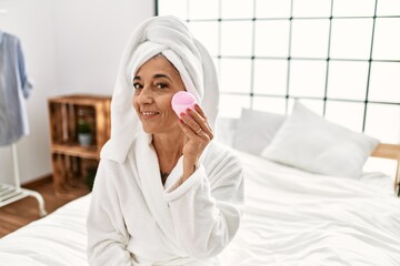 Middle age grey-haired woman cleaning skin face sitting on bed at bedroom