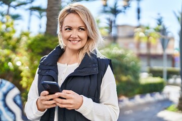 Fototapeta premium Young blonde woman smiling confident using smartphone at park