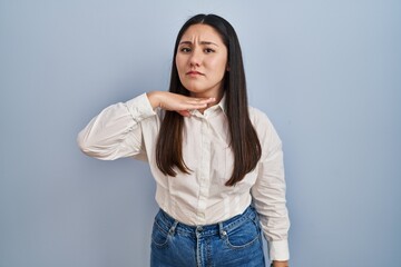 Young latin woman standing over blue background cutting throat with hand as knife, threaten aggression with furious violence