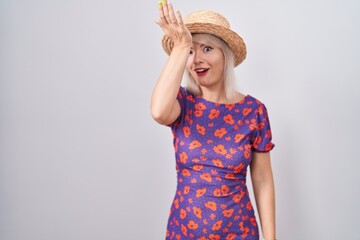 Young caucasian woman wearing flowers dress and summer hat surprised with hand on head for mistake, remember error. forgot, bad memory concept.