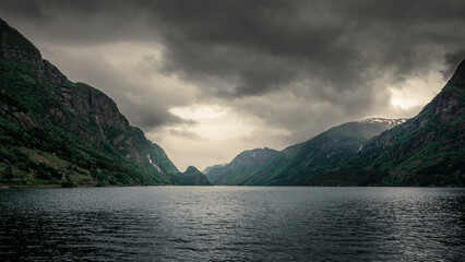 Norwegian fjord with waterfall in the mountains and dark moody clouds in the sky
