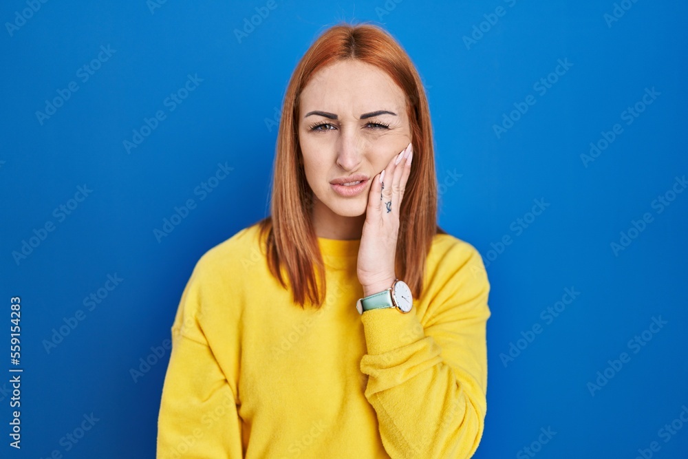 Wall mural Young woman standing over blue background touching mouth with hand with painful expression because of toothache or dental illness on teeth. dentist