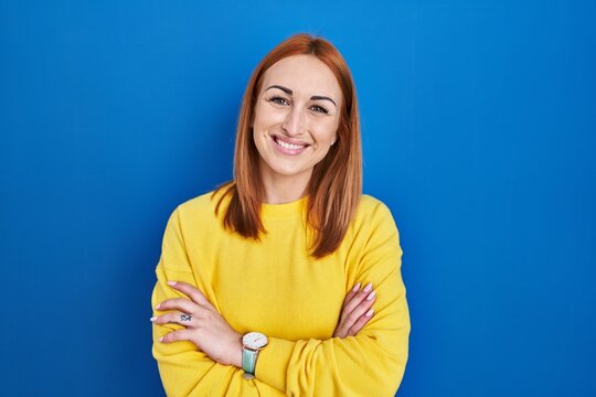 Young woman standing over blue background happy face smiling with crossed arms looking at the camera. positive person.