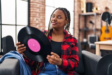 African american woman musician smiling confident holding vinyl disc at music studio