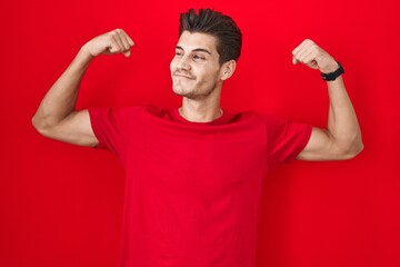 Young hispanic man standing over red background showing arms muscles smiling proud. fitness concept.