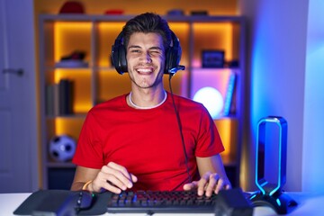 Young hispanic man playing video games winking looking at the camera with sexy expression, cheerful...
