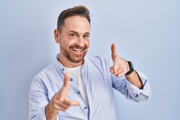 Middle age caucasian man standing over blue background pointing fingers to camera with happy and funny face. good energy and vibes.