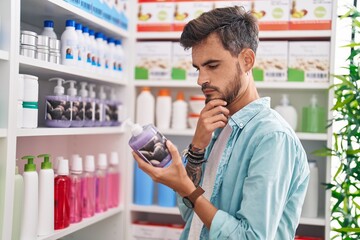 Young hispanic man customer reading label gel hands bottle at pharmacy