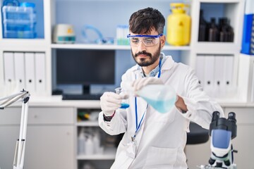 Young hispanic man scientist pouring liquid on glass at laboratory