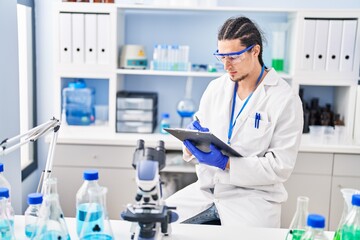 Young man wearing scientist uniform write on clipboard at laboratory