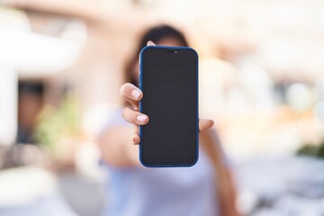 Young hispanic woman showing smartphone screen at street