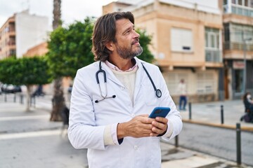 Middle age man doctor smiling confident using smartphone at street