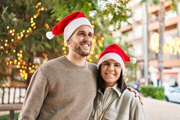 Man and woman couple wearing christmas hat hugging each other at park