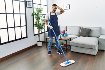 Young hispanic man tired cleaning floor using mop at home