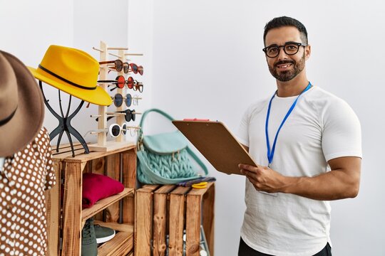 Young hispanic man shopkeeper writing on checklist working at clothing store