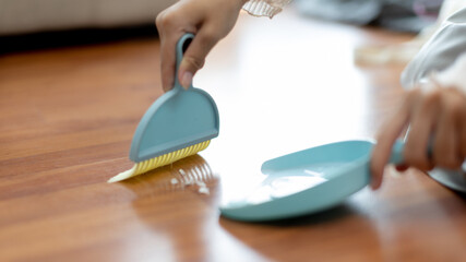 Close-up shot of hand holding a broom, Scooping rubbish into the dustpan, Cleaning scraps of paper on a wooden floor, Scouring, Broom and dustpan, Big cleaning concept.