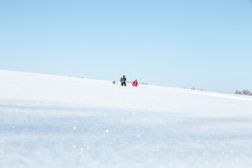 Naklejka na ściany i meble Two silhouettes of children in blue and red overalls against a clear blue sky. People on the horizon. The children went into the distance on clear white snow. .Soft focus. Blured. Film Grain Defocused