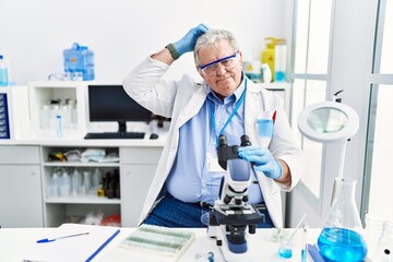 Naklejka na ściany i meble Senior caucasian man working at scientist laboratory confuse and wondering about question. uncertain with doubt, thinking with hand on head. pensive concept.