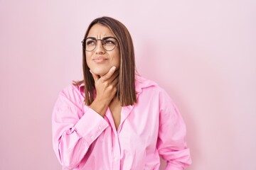 Fototapeta premium Young hispanic woman wearing glasses standing over pink background touching painful neck, sore throat for flu, clod and infection