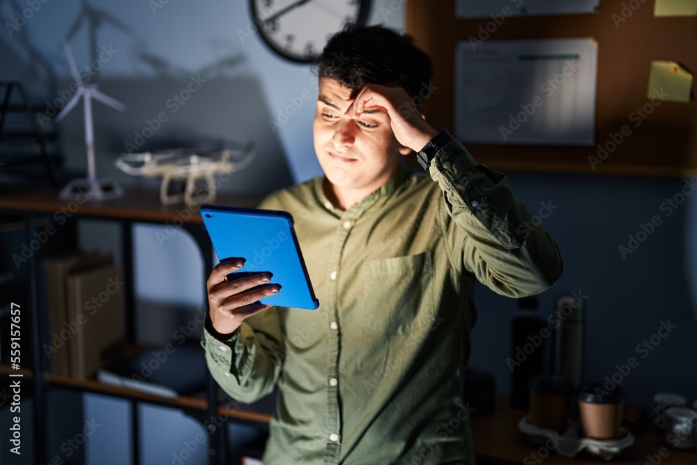 Wall mural Non binary person using touchpad device at night worried and stressed about a problem with hand on forehead, nervous and anxious for crisis