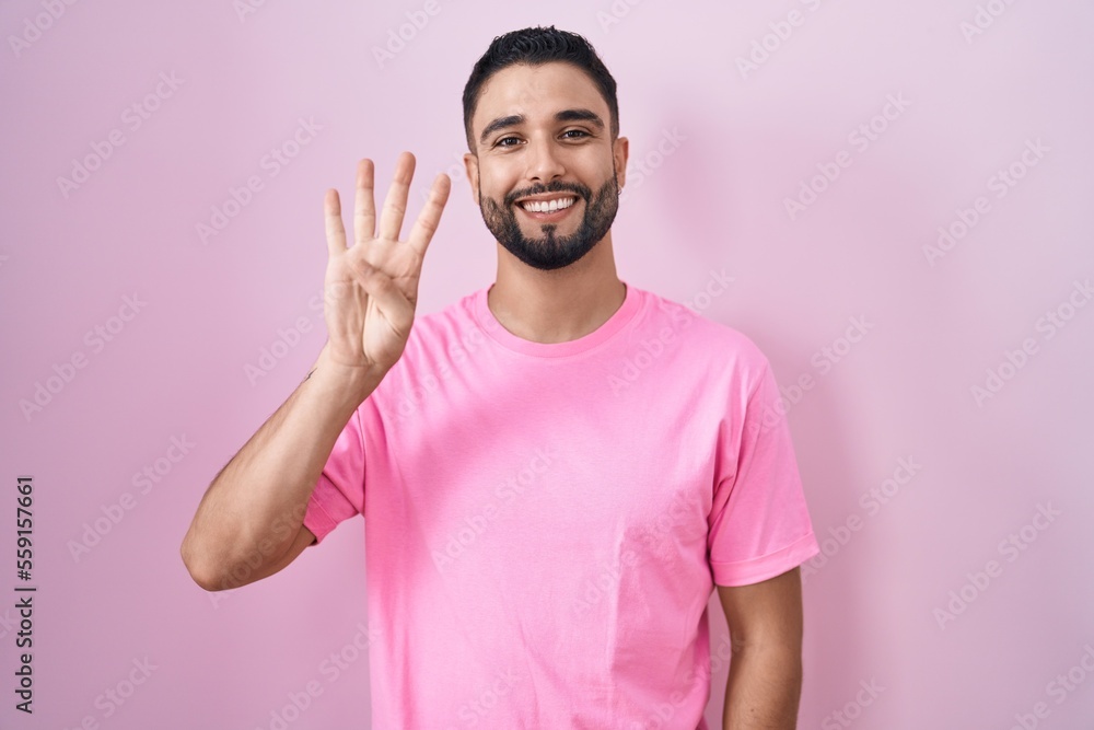 Canvas Prints Hispanic young man standing over pink background showing and pointing up with fingers number four while smiling confident and happy.