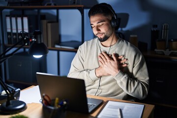 Young handsome man working using computer laptop at night smiling with hands on chest with closed eyes and grateful gesture on face. health concept.