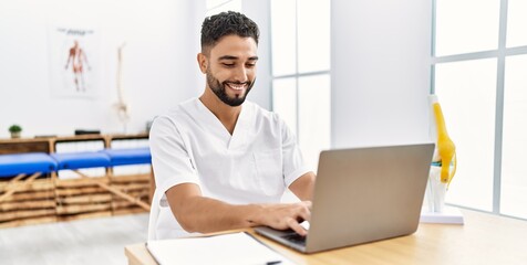 Young arab man wearing physiotherapist uniform using laptop at clinic