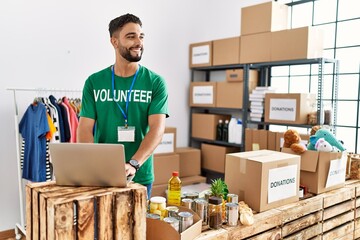 Young arab man wearing volunteer uniform using laptop at charity center