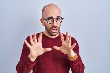 Naklejka premium Young bald man with beard standing over white background wearing glasses afraid and terrified with fear expression stop gesture with hands, shouting in shock. panic concept.