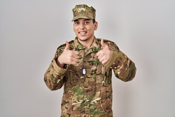 Young arab man wearing camouflage army uniform success sign doing positive gesture with hand, thumbs up smiling and happy. cheerful expression and winner gesture.