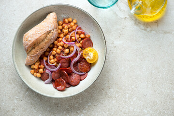 Plate of chorizo and chickpea stew on a beige stone background, horizontal shot with copy space, flat lay