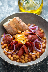Bowl of tomato stew with chickpeas, fried chorizo sausage and red onion, vertical shot, close-up