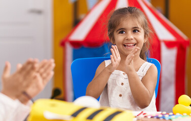 Adorable hispanic girl sitting on table applauding at kindergarten