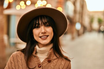 Brunette woman wearing winter hat smiling outdoors at the city
