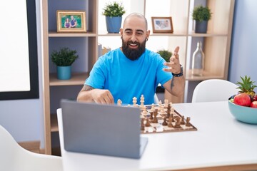 Young bald man playing online chess game sitting on table at home