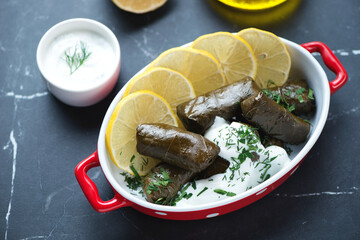 Red serving bowl with turkish sarma, white yogurt and lemon, horizontal shot on a black marble background