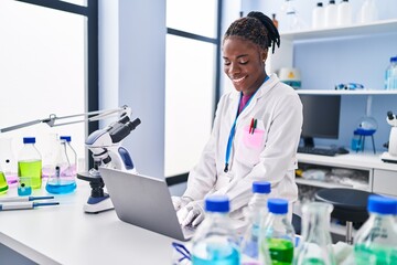African american woman wearing scientist uniform using laptop at laboratory