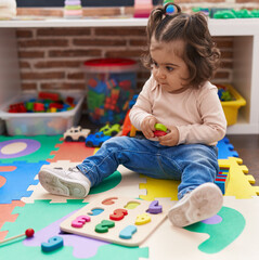 Adorable hispanic girl playing with maths puzzle game sitting on floor at kindergarten