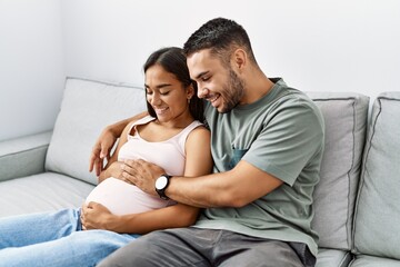 Latin man and woman couple hugging each other expecting baby at home